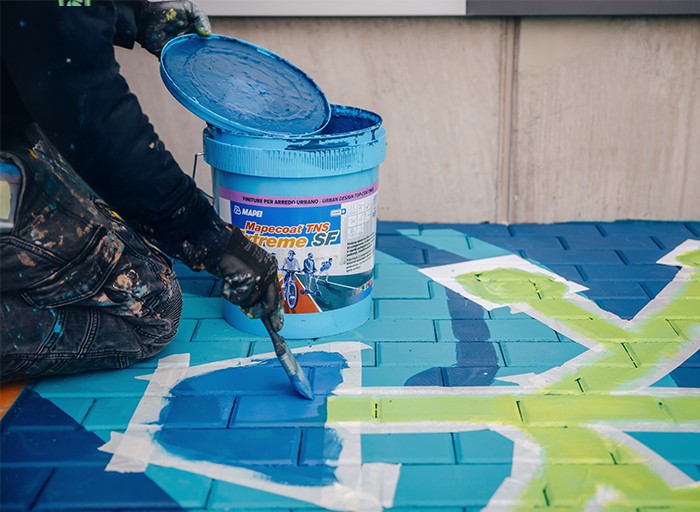 Přenos symbolu recyklace pomocí šablony na barevně upravený chodník.