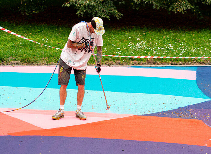 Umělec natírá barevné tvary na betonový povrch pomocí spreje a šablon.