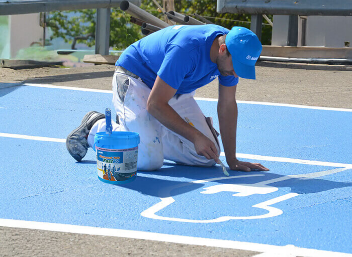 Aplikace bílého značení na modrý sportovní povrch pomocí Mapecoat TNS Fast.